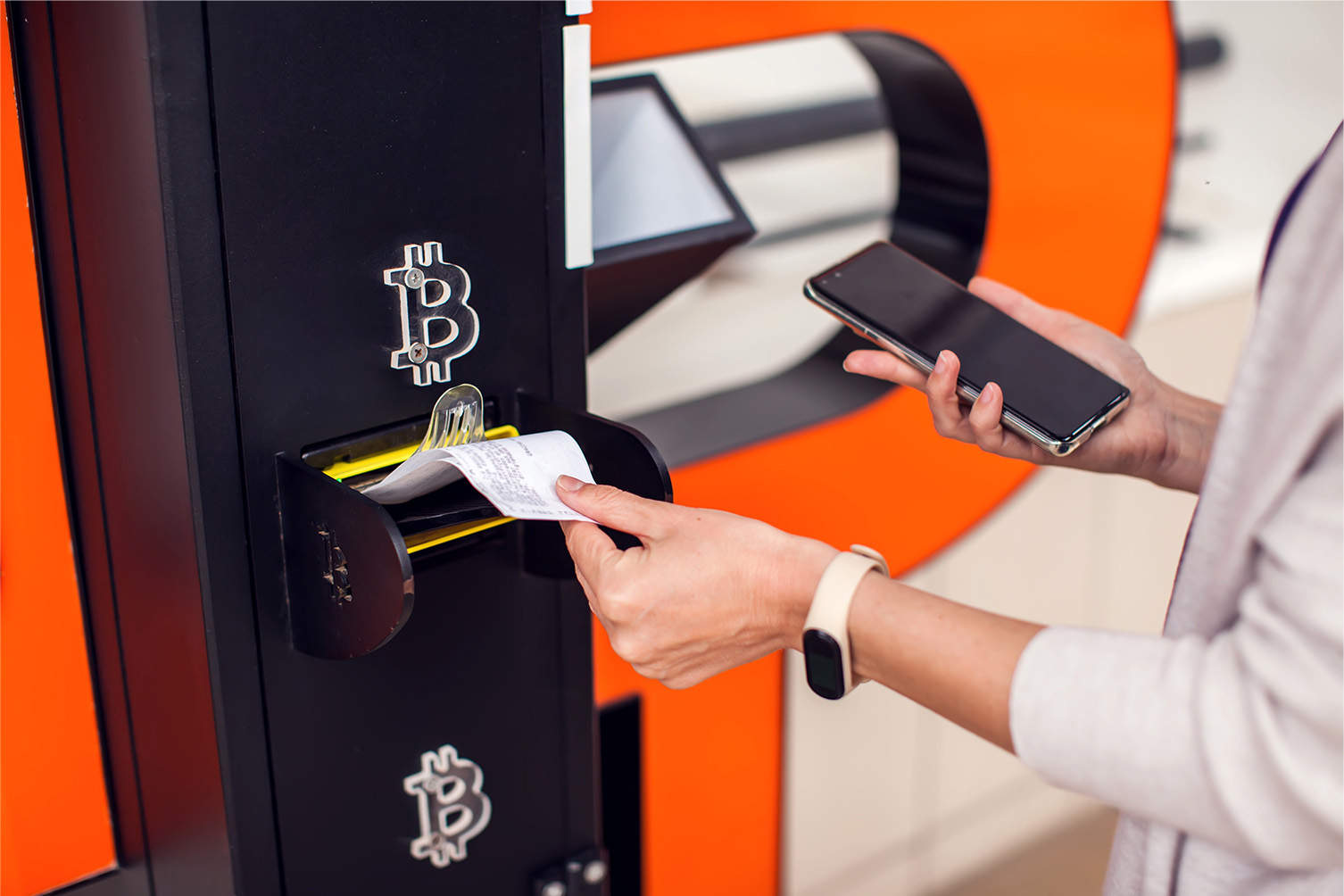 A woman’s hand grabbing a piece of paper from a machine with the Bitcoin symbol